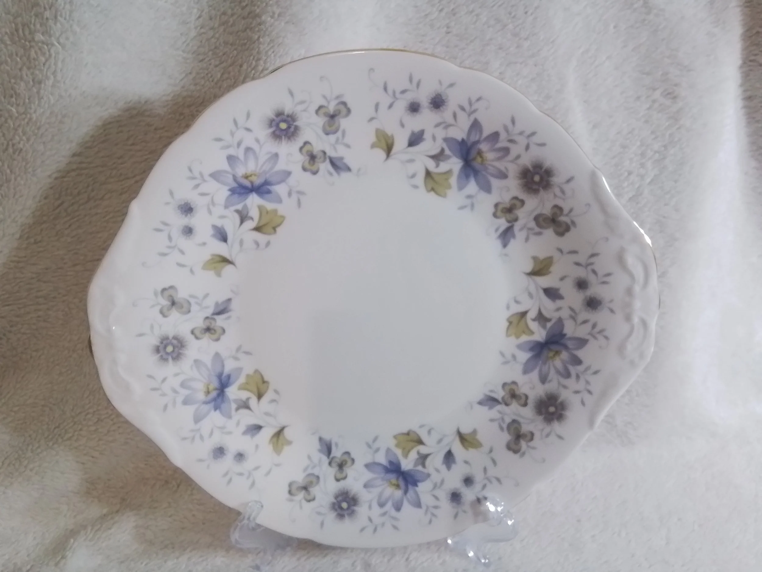 A decorative porcelain plate with a floral pattern of purple, blue, and gold flowers along the rim, resting on a beige fabric surface.