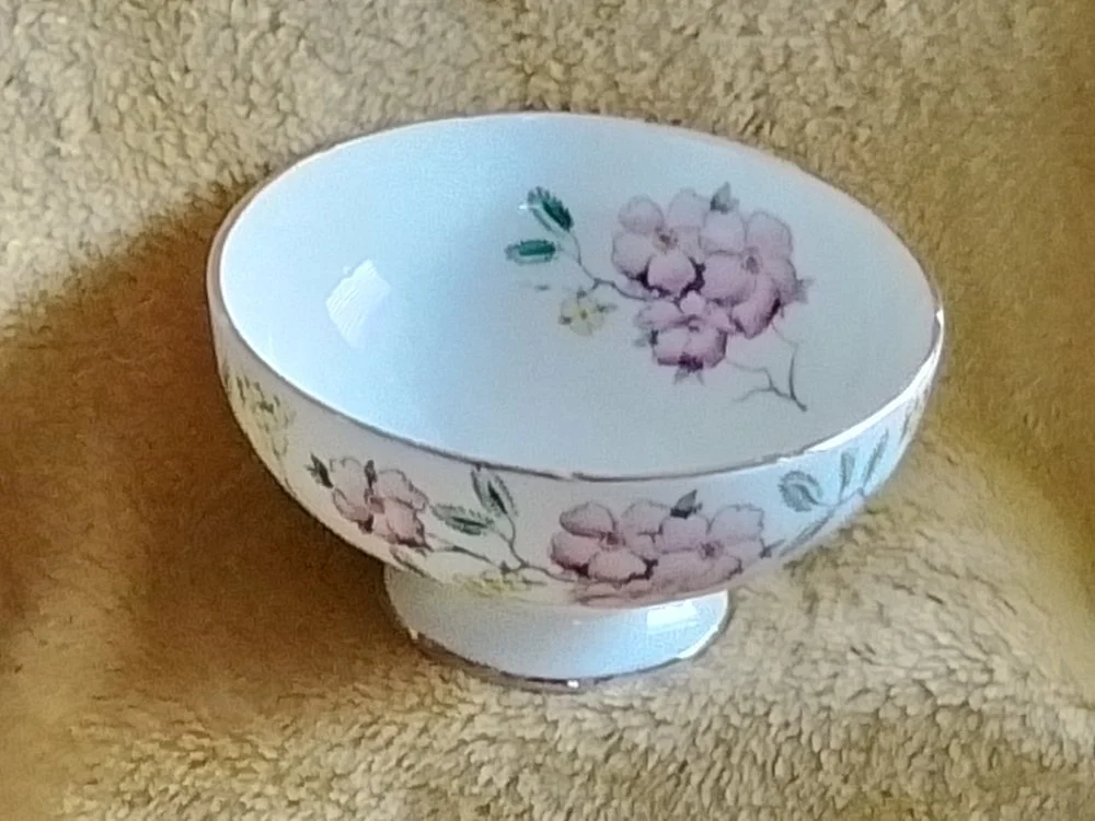 A porcelain bowl with pink and purple floral pattern on a beige textured surface.