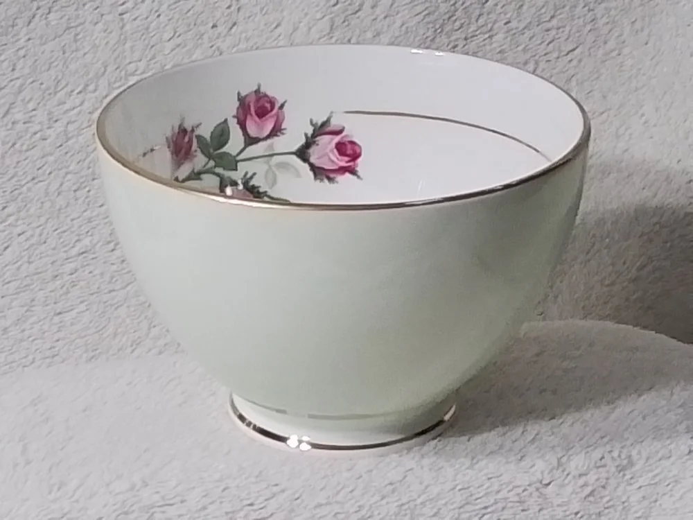 A white ceramic bowl with pink roses and green leaves design on the inside rim, placed on a light textured surface.