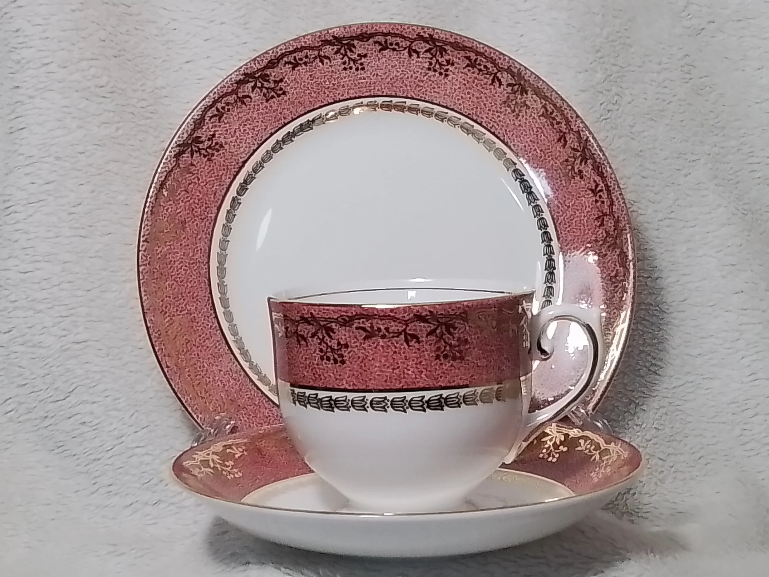 A decorative porcelain teacup, saucer, and plate with a pink and gold floral pattern.