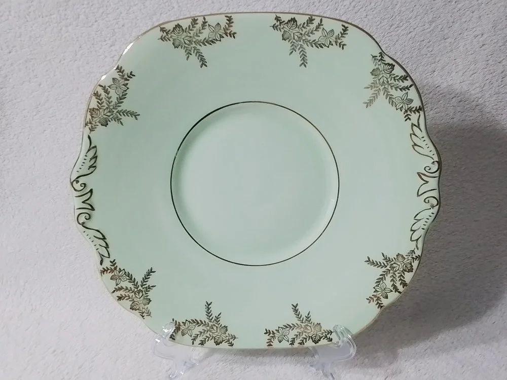 A decorative porcelain plate with scalloped edges and a gold and dark green leafy pattern around the border.