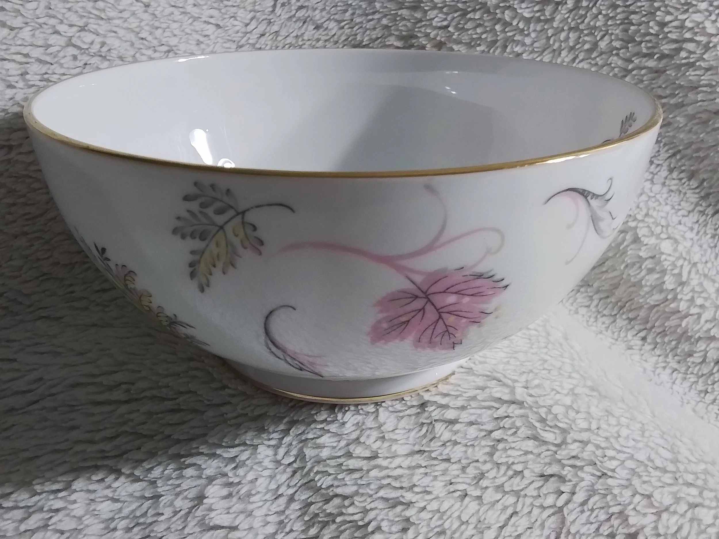 White porcelain bowl with floral and leaf design, gold trim, placed on a textured white surface.