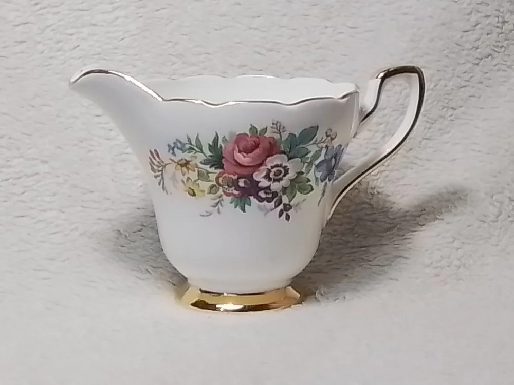 A porcelain teapot with a floral design, gold accents, and a curved handle.