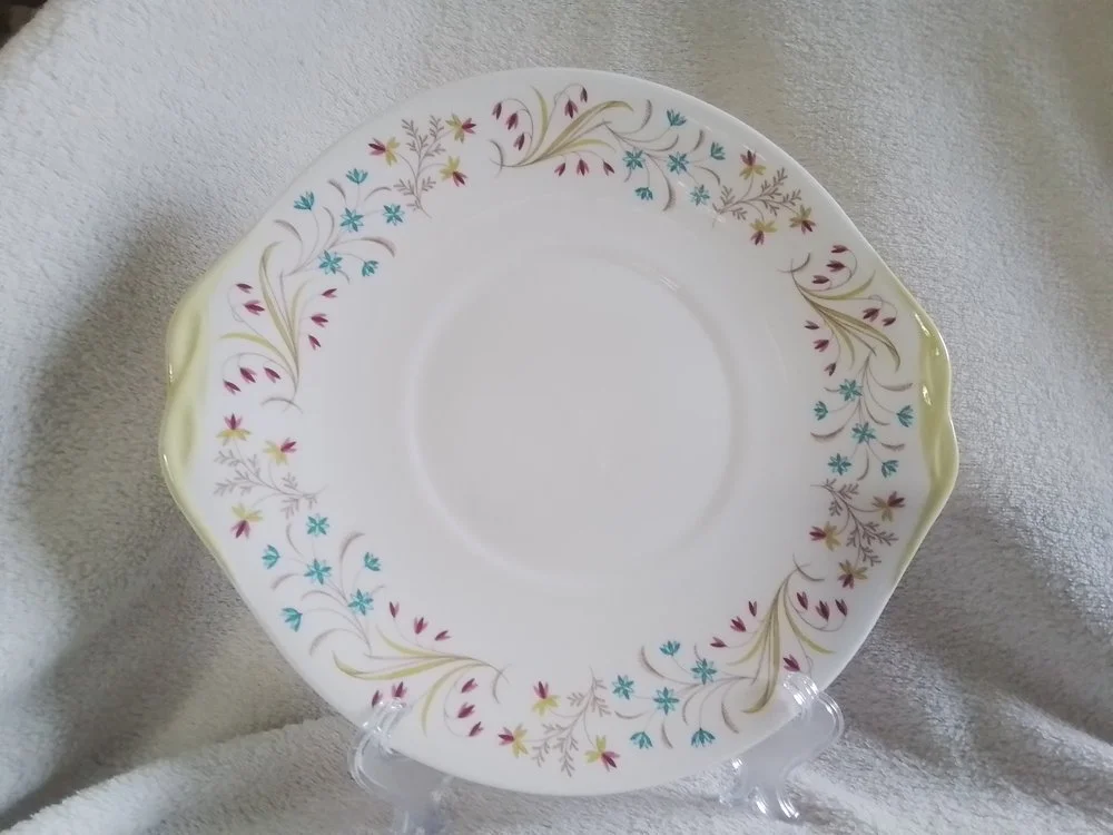 A white decorative plate with a floral pattern of small, colorful flowers and leaves around the rim, displayed on a clear stand.
