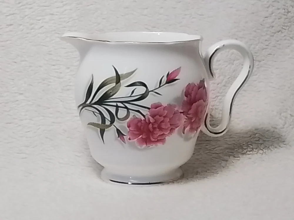 White porcelain creamer with floral design of pink flowers and green leaves.