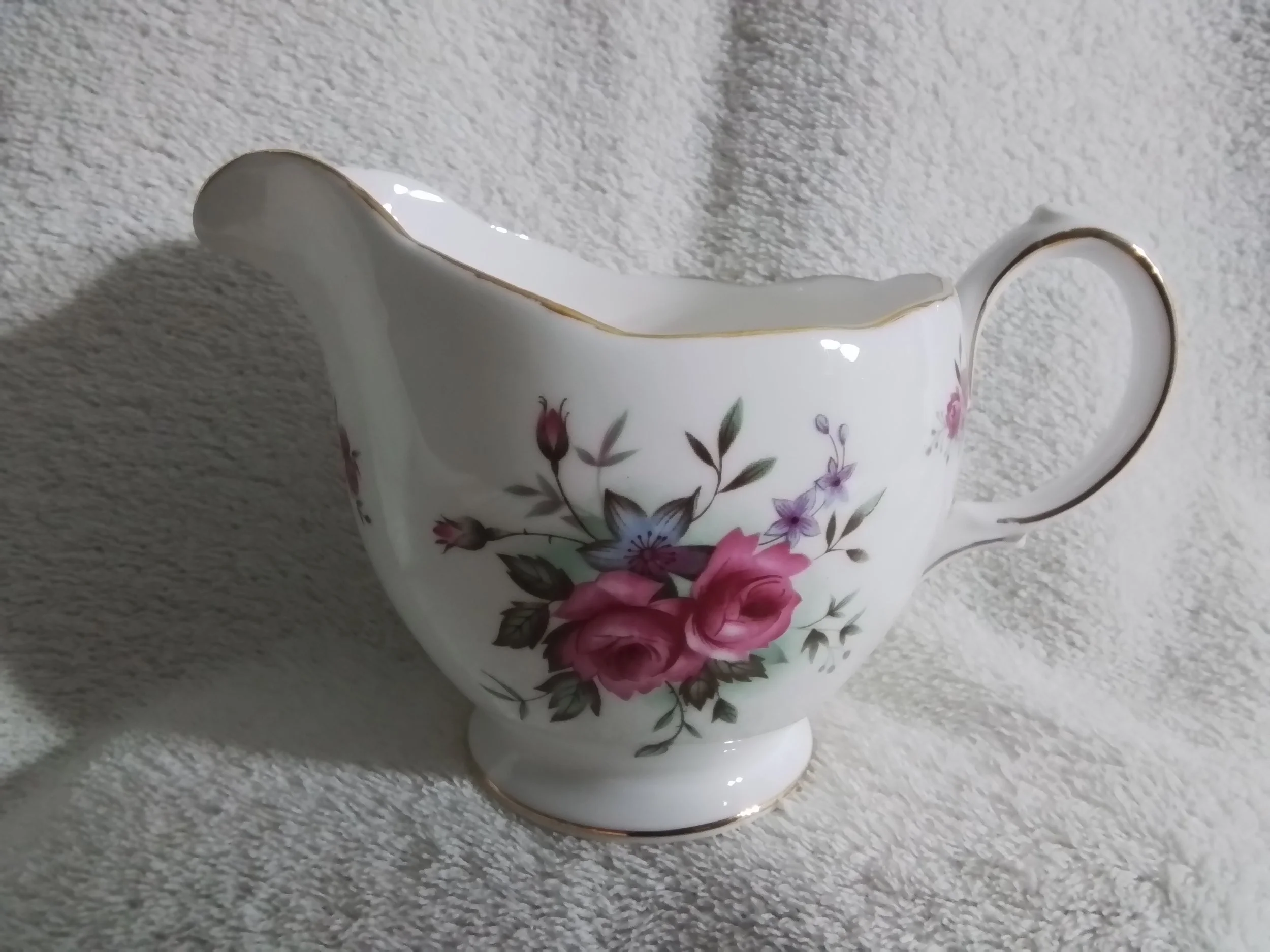 A porcelain gravy boat with a floral design of pink and purple flowers and green leaves, edged in gold.