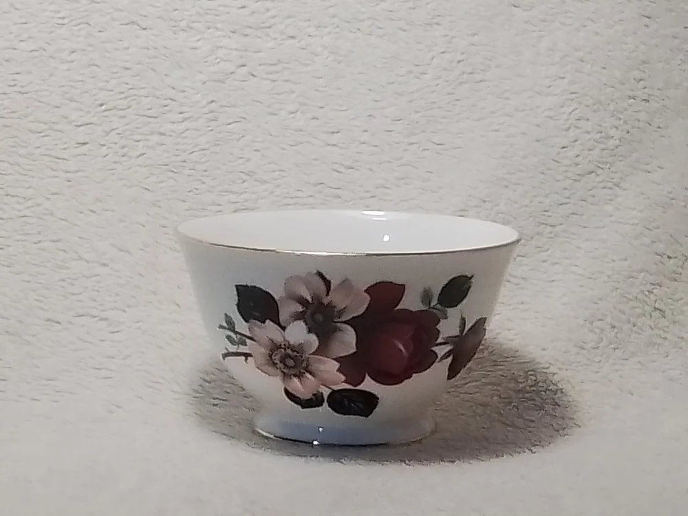 A white ceramic bowl with a floral pattern of pink, purple, and green flowers and leaves, sitting on a textured white surface.