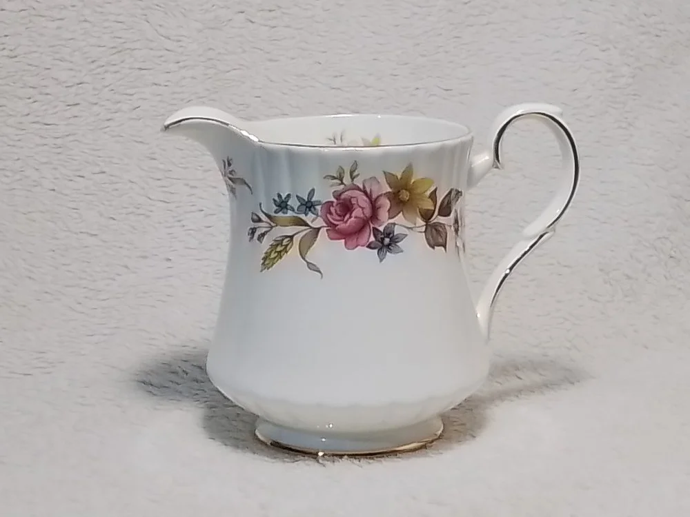 A white ceramic creamer with floral pattern including pink, yellow, and blue flowers and green leaves.