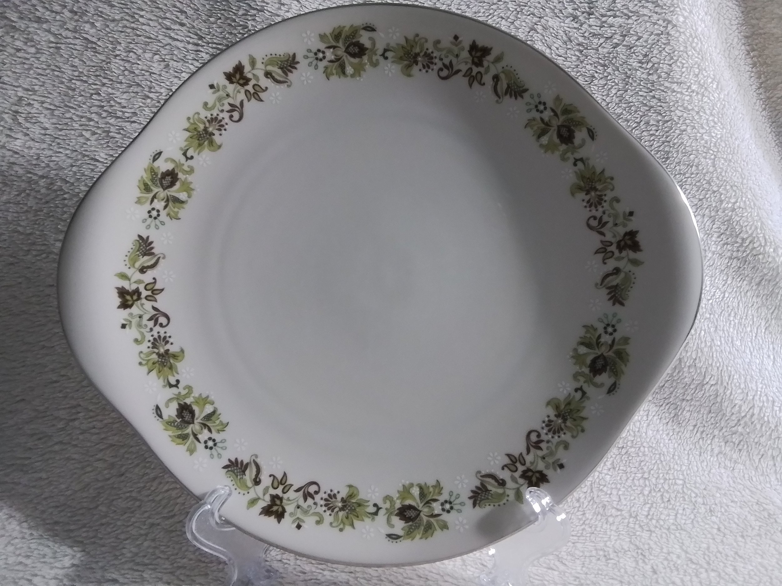 White square ceramic plate with a floral green and brown pattern around the rim, set on a textured light-colored surface.