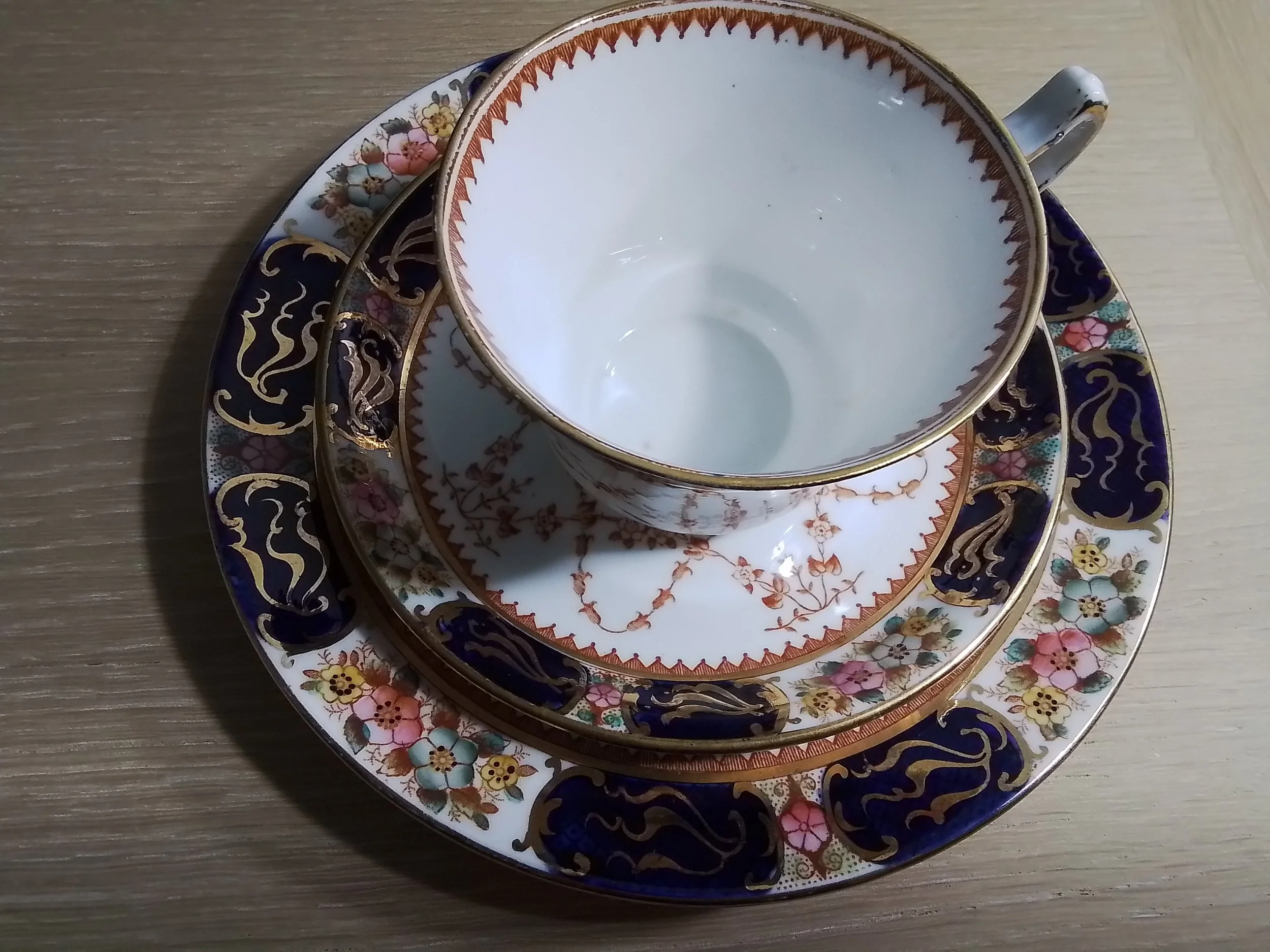 A stack of ornate porcelain teacups and saucers with floral and gold patterns on a wooden surface.