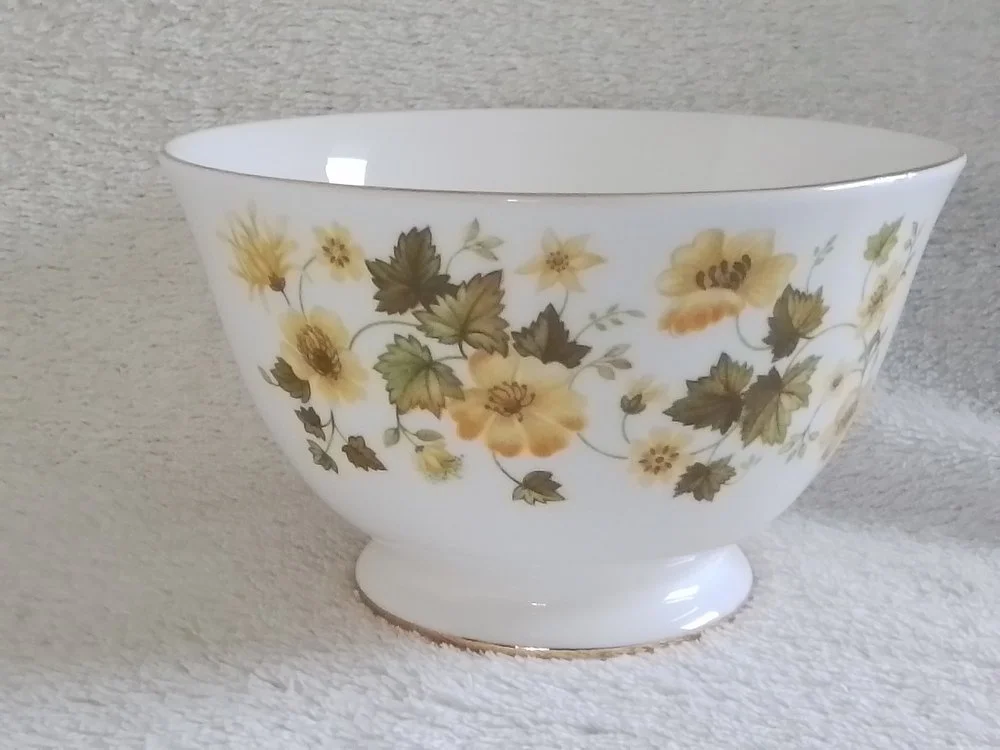 White porcelain bowl with yellow flower and green leaf floral pattern.
