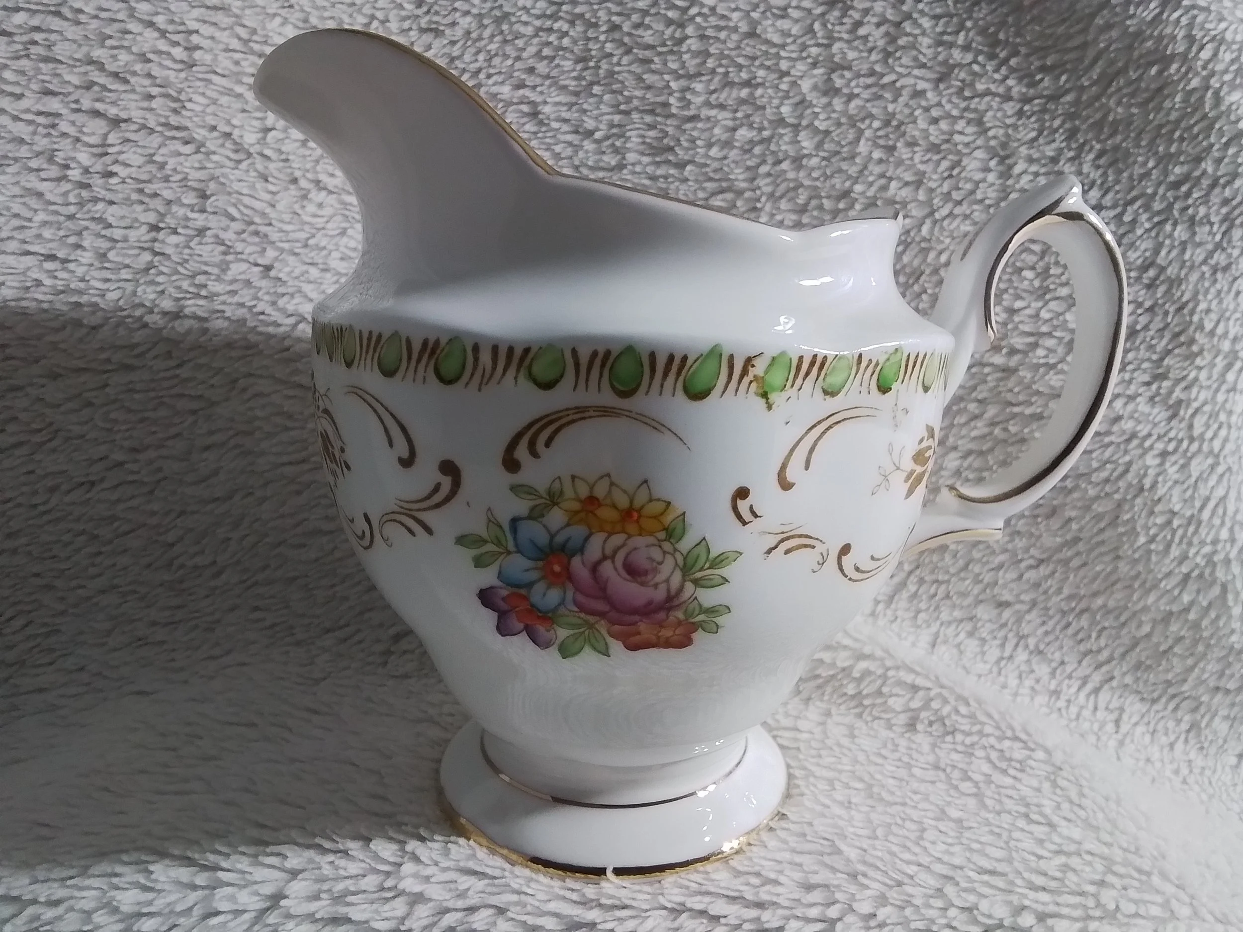 A decorative ceramic gravy boat with floral patterns and gold accents on a textured white background.