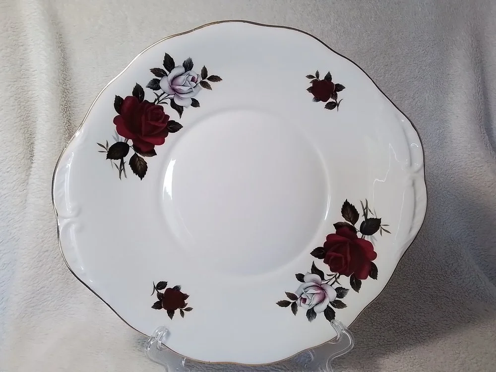 A decorative porcelain plate with a floral pattern of red and white roses with green leaves, outlined with a gold trim.