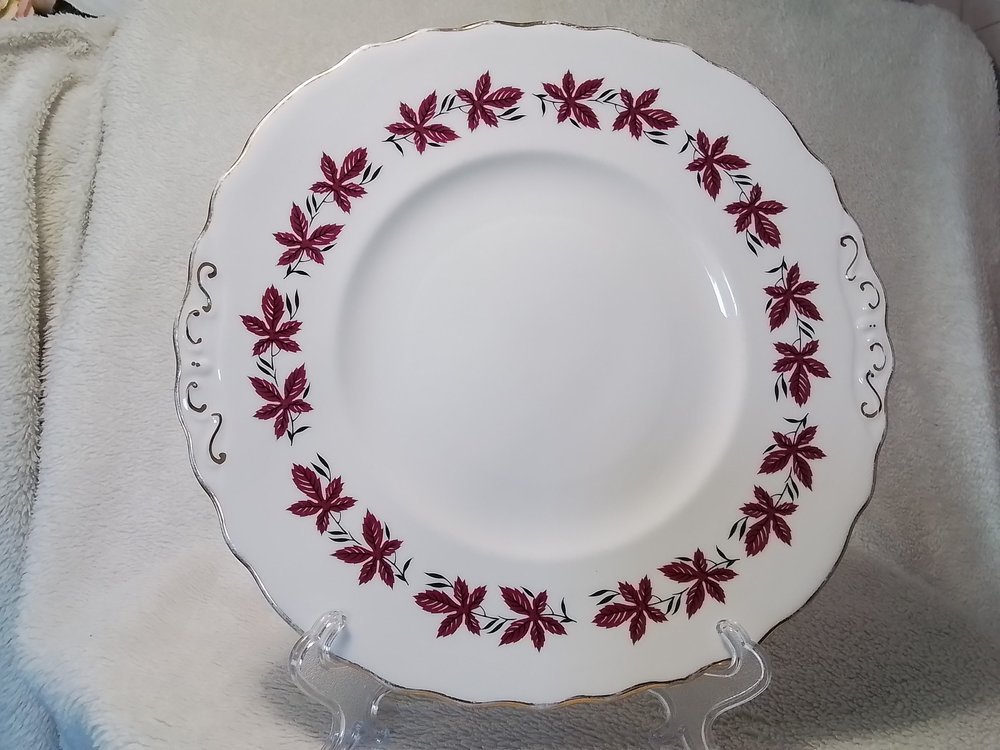 A decorative white ceramic plate with a red and black floral pattern around the rim, displayed on a clear stand.