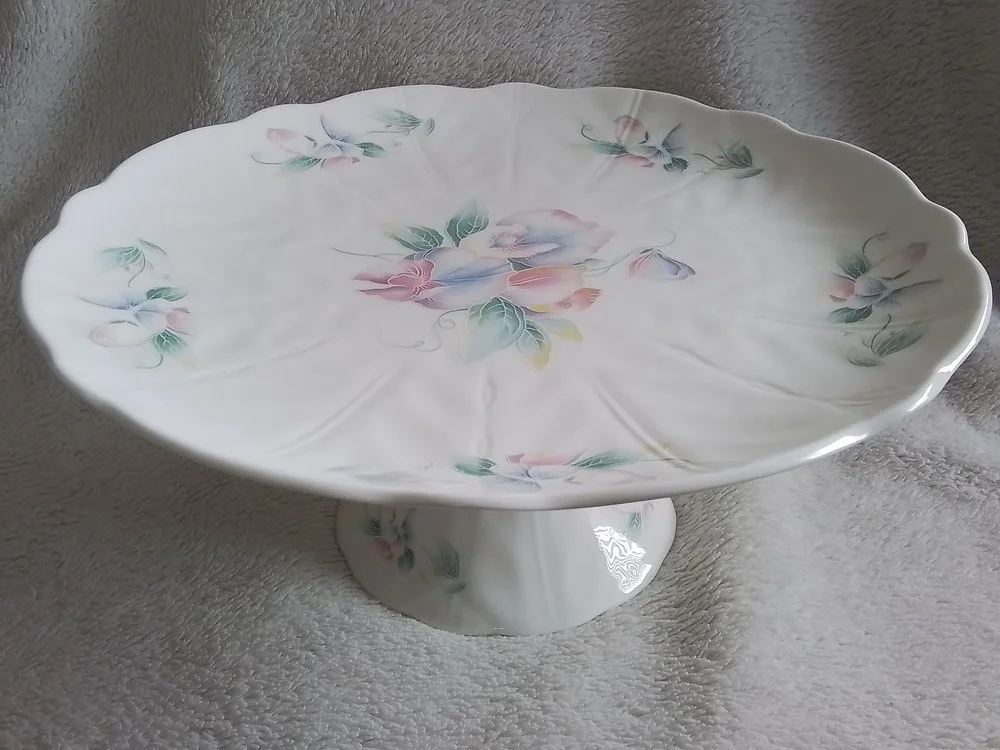 A decorative porcelain cake stand with a floral pattern, set on a gray surface.