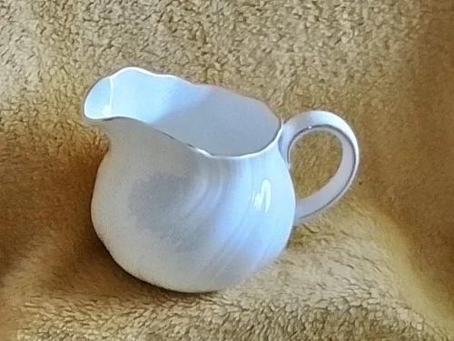 White ceramic creamer jug on a yellow textured surface.