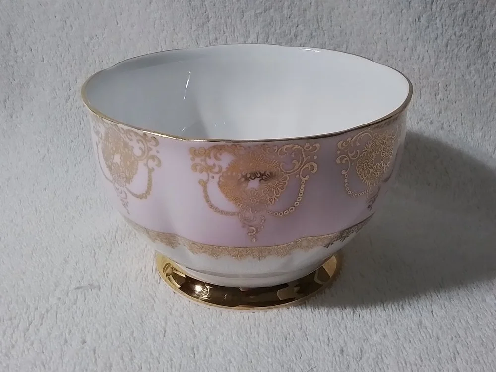 A decorative porcelain bowl with gold floral patterns and a gold rim, placed on a white textured surface.