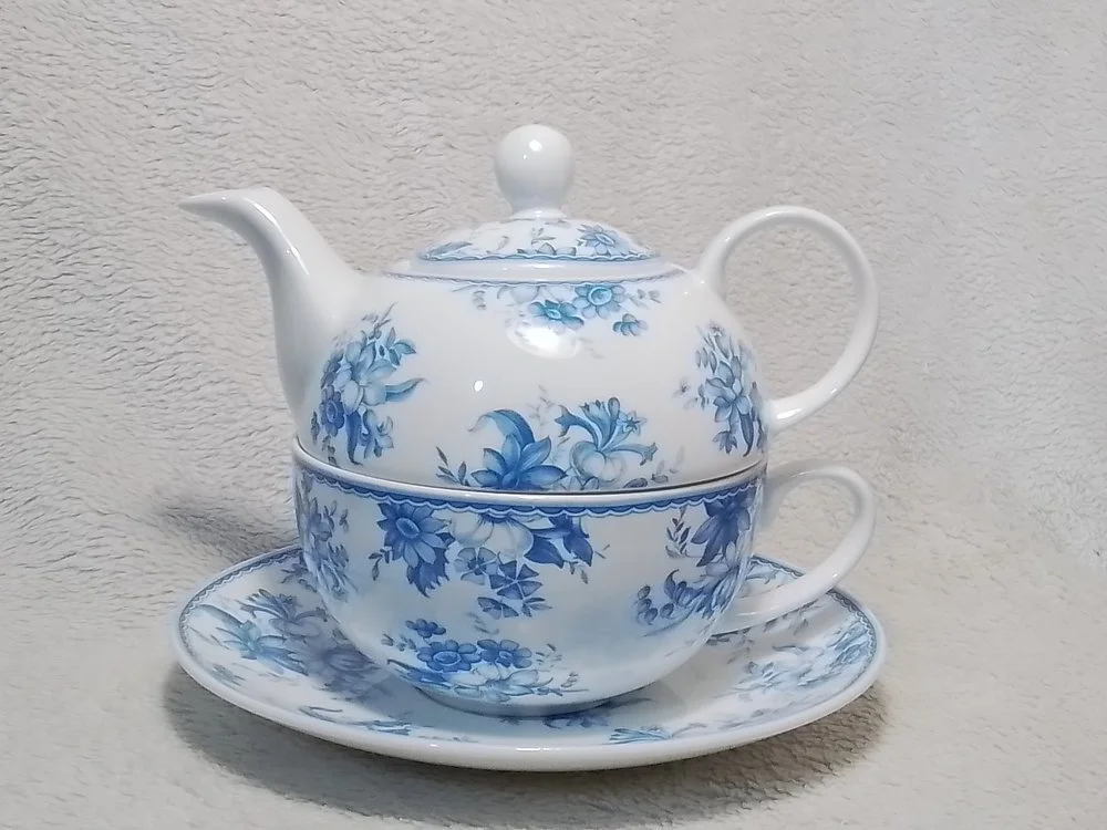 A white and blue floral patterned porcelain teapot stacked on a matching teacup with a saucer underneath.