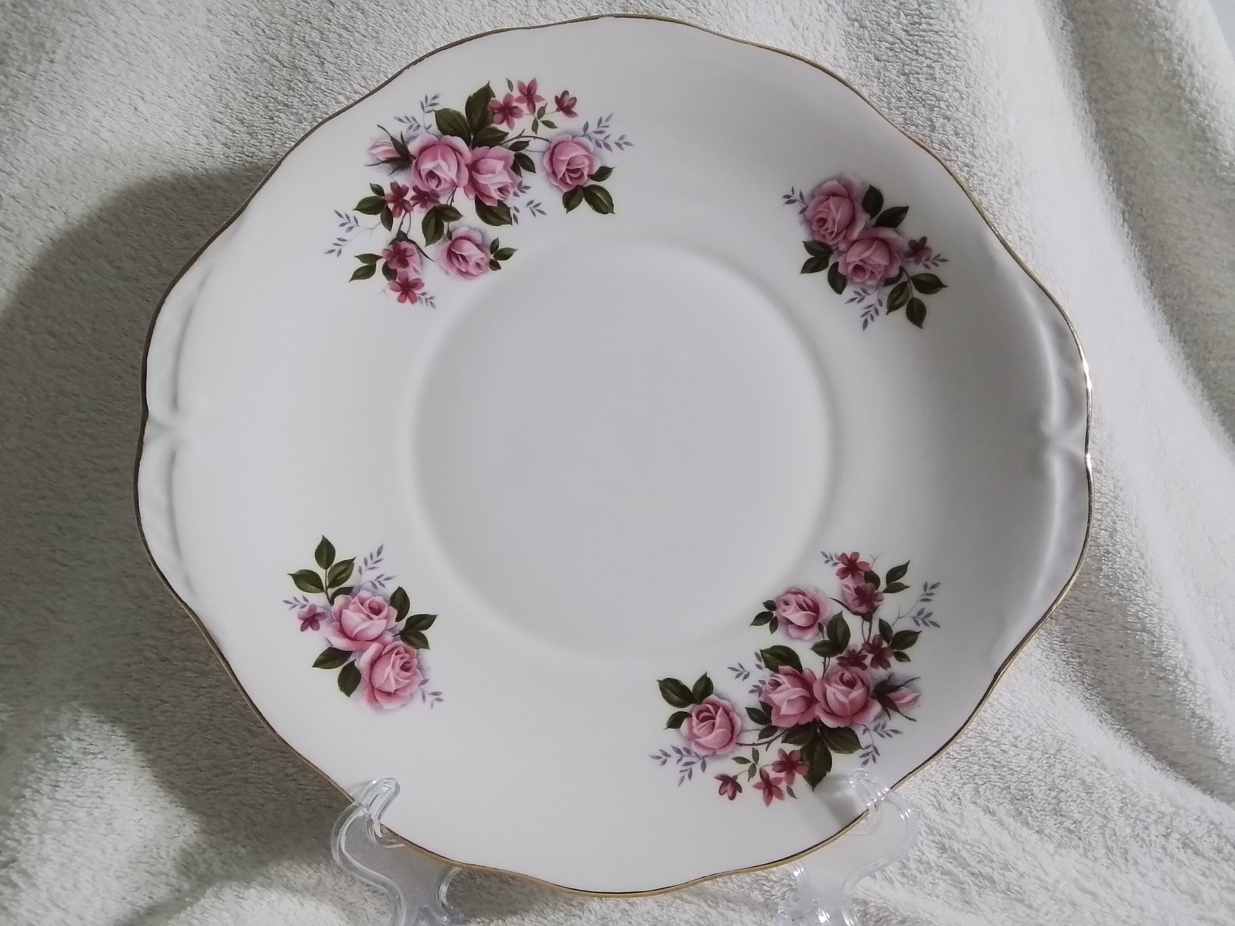 White decorative plate with pink rose floral border and gold trim on a white textured surface.