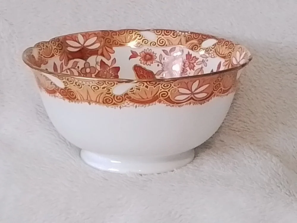 Decorative porcelain bowl with gold floral and swirl pattern on the rim, placed on a textured white surface.