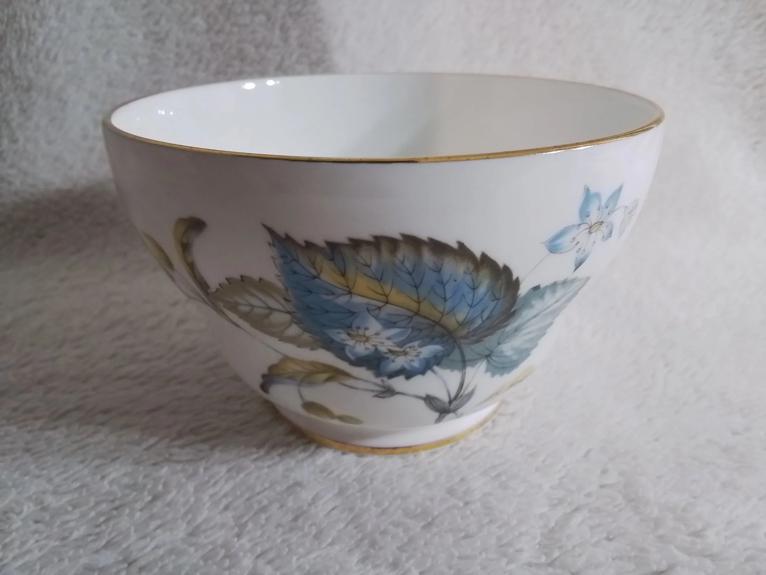 A white porcelain bowl with a gold rim and floral design featuring blue and yellow leaves and flowers.