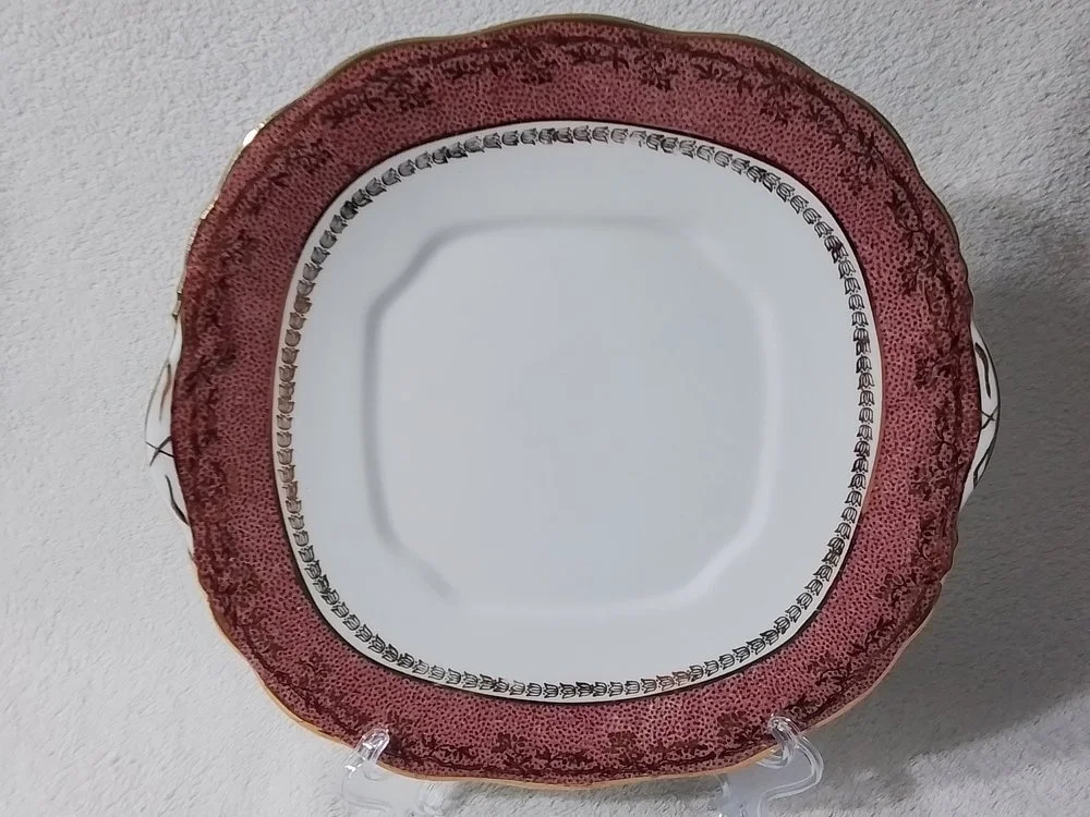Decorative ceramic plate with a red and white pattern, displayed on a clear stand against a white background.