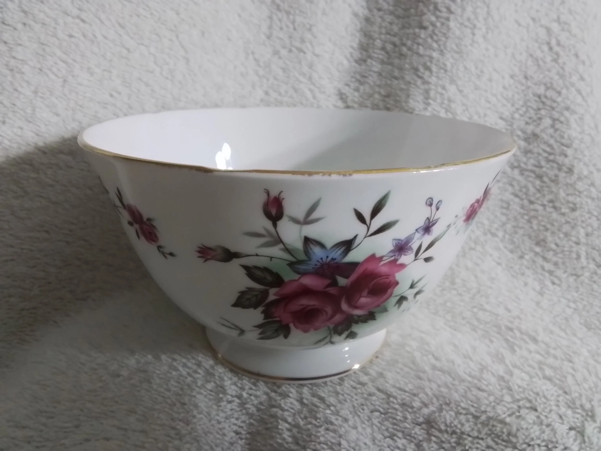 A white ceramic bowl with a floral pattern of pink roses, purple flowers, and green leaves, placed against a textured white background.