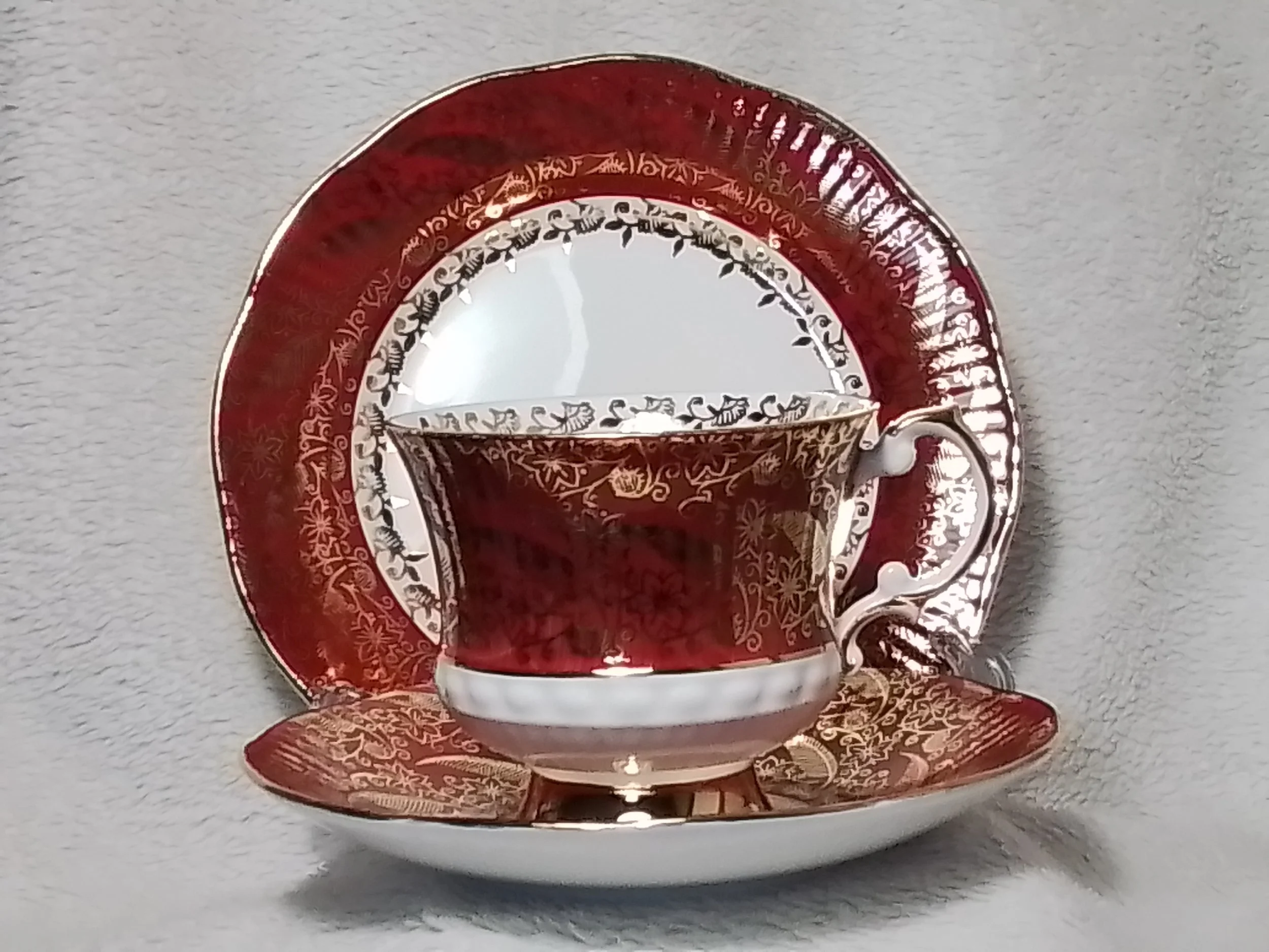 A porcelain teacup and saucer with red, gold, and white intricate floral and geometric patterns.