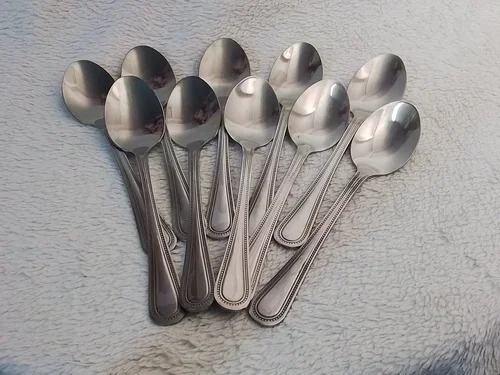 Set of ten stainless steel teaspoons arranged on a textured surface.