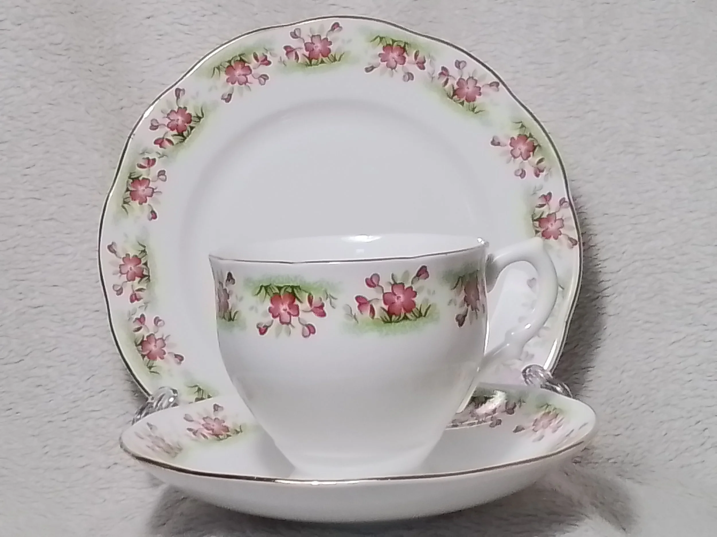 A decorative porcelain teacup and saucer set with pink floral pattern, with a matching large plate behind them, all placed on a light-colored textured surface.