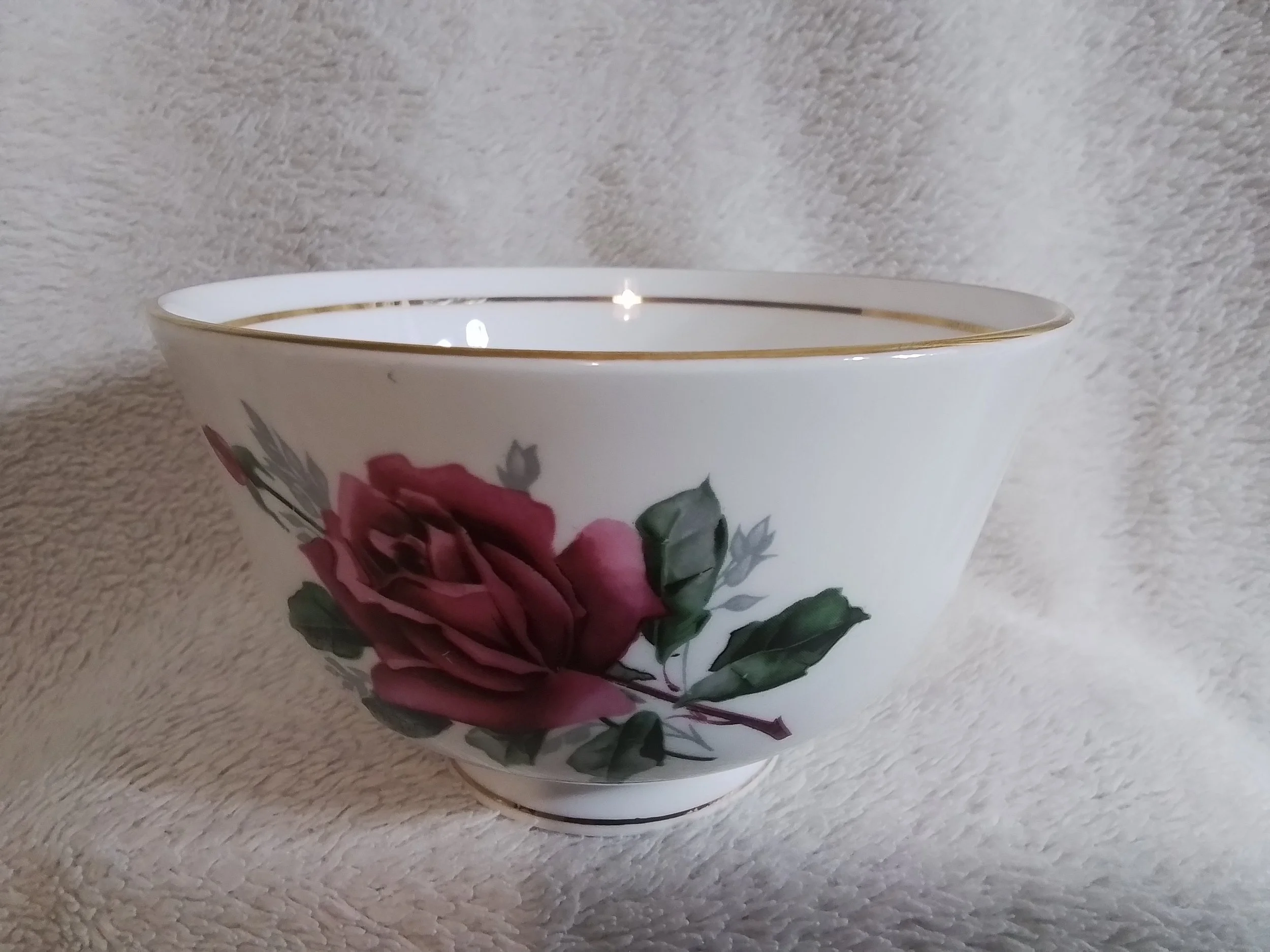 A white porcelain bowl with a pink rose and green leaves design and a gold rim.