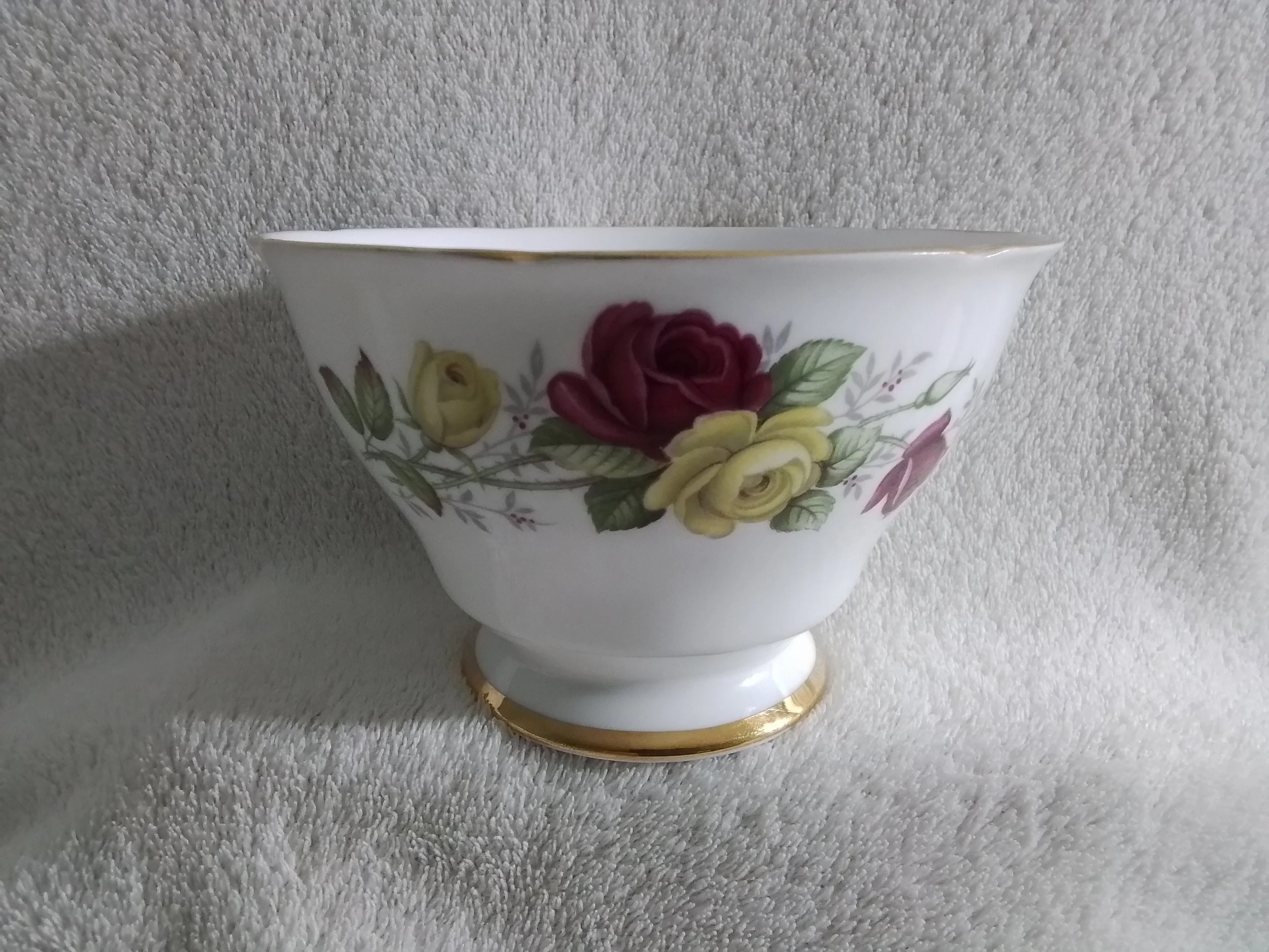 A porcelain flower-shaped bowl with gold rim and floral pattern featuring yellow, red, and pink roses with green leaves.