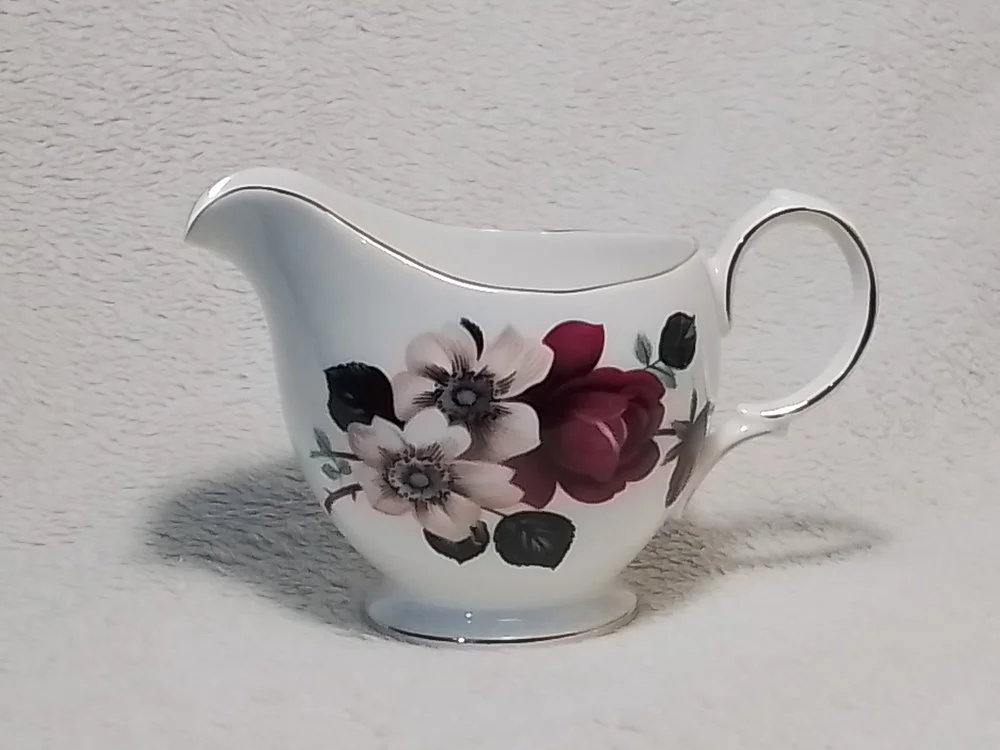 A white porcelain creamer with floral design, featuring pink and white flowers with green leaves.