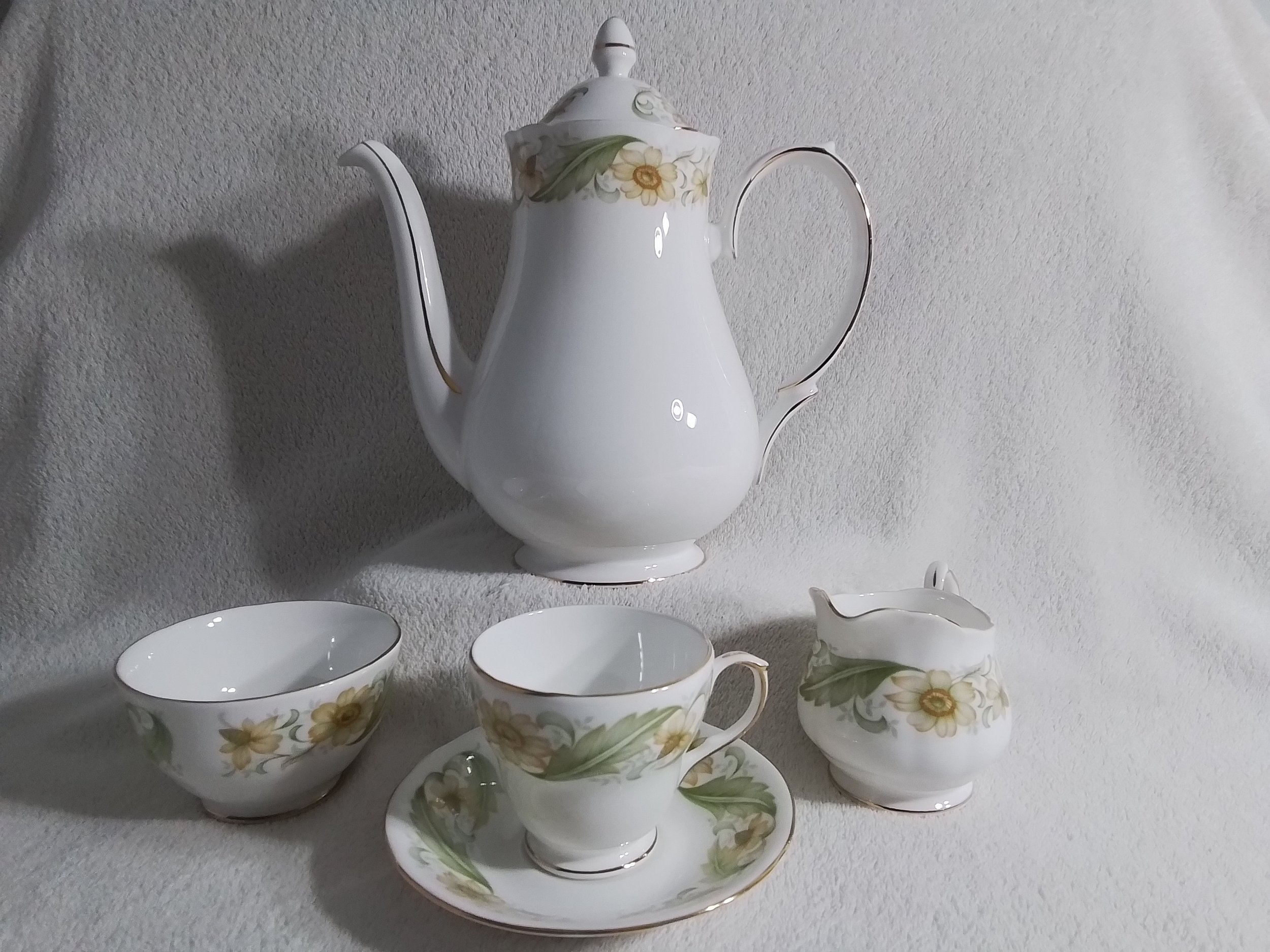 A white porcelain teapot with floral design, accompanied by matching cups and creamer, set against a light textured background.