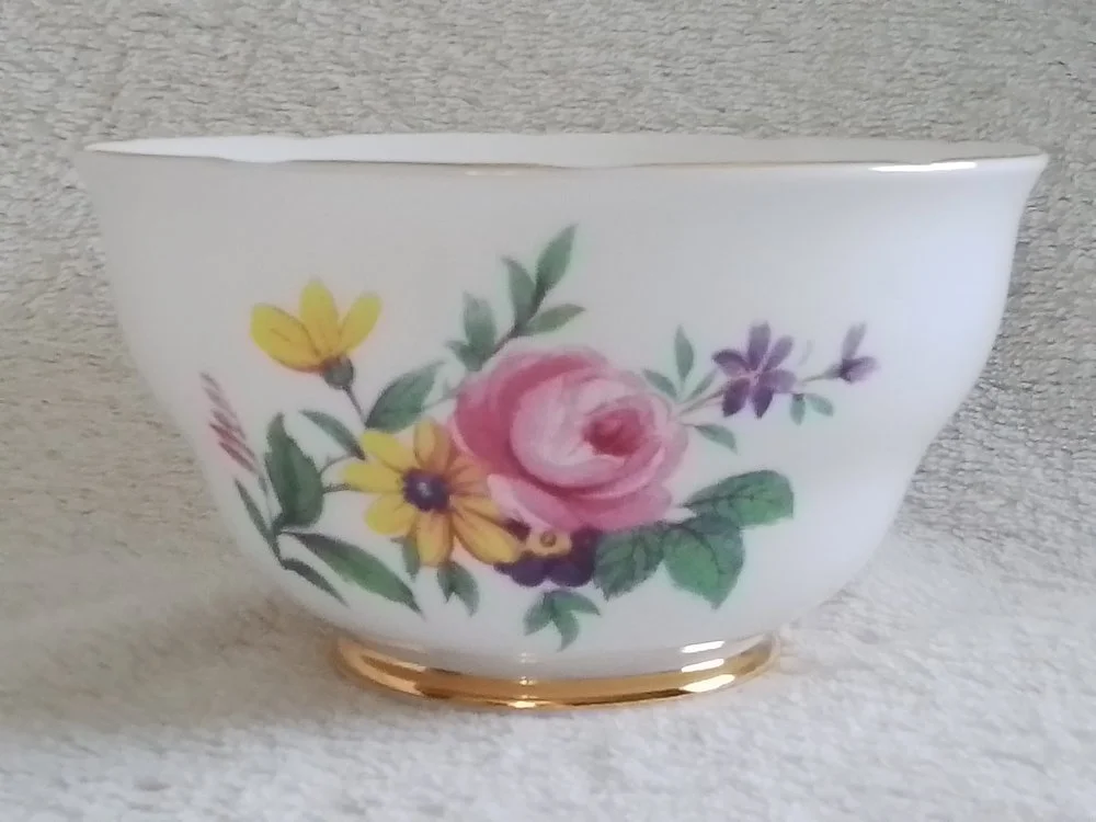A white ceramic bowl with floral design, including pink, yellow, purple flowers, and green leaves, and a gold trim at the base.