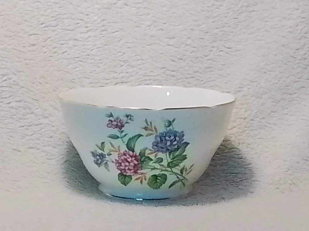 A white ceramic bowl with a floral pattern of pink, purple, and blue flowers and green leaves, placed on a textured white surface.