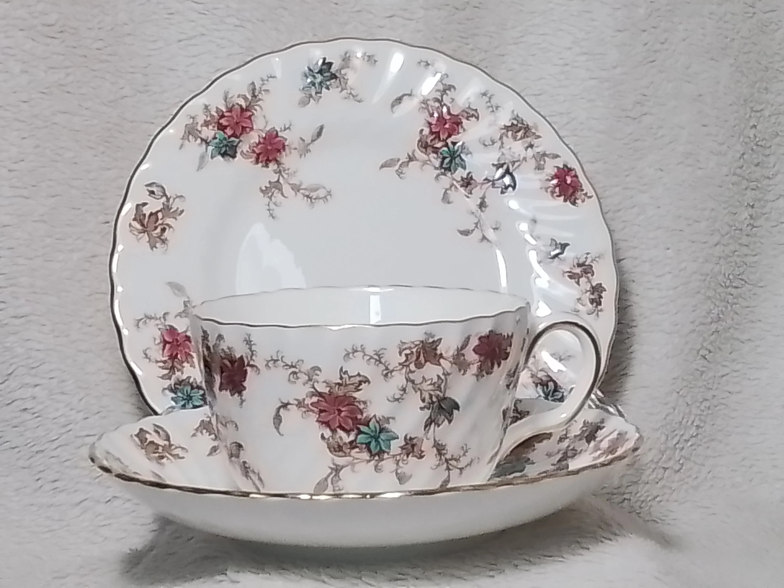 Decorative porcelain teacup with floral pattern, resting on a matching saucer, against a soft, light-colored textured background.