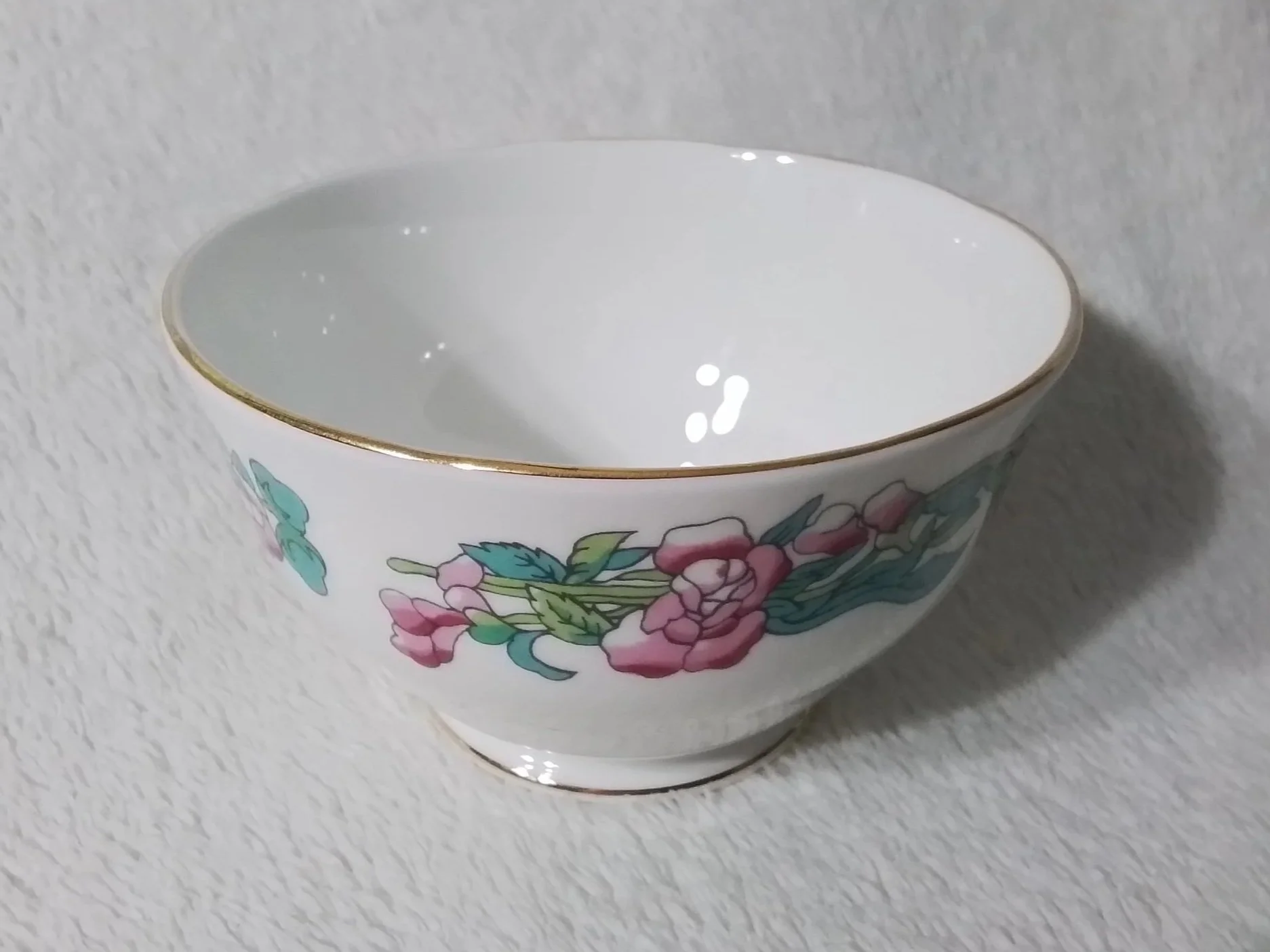 A white porcelain bowl with gold rim and pink floral pattern on the side, placed on a textured white surface.