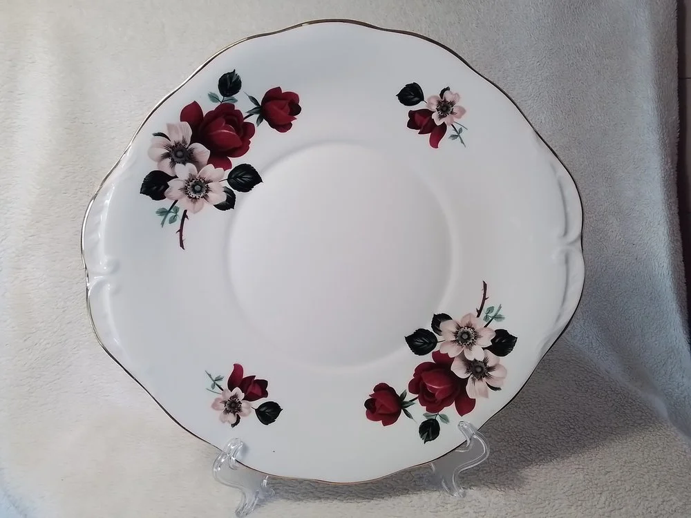 A decorative ceramic plate with floral patterns in black, white, and burgundy, featuring a scalloped edge with a thin gold rim.
