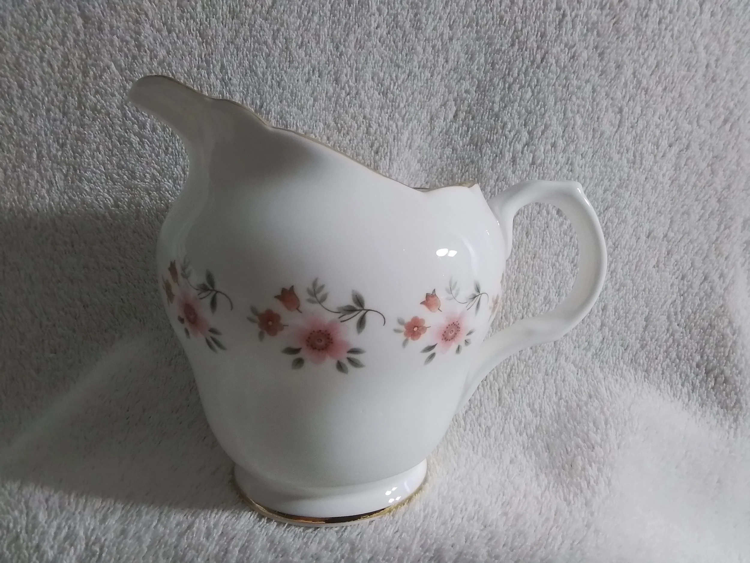White porcelain pitcher with pink and gray floral pattern, set on a light textured fabric background.