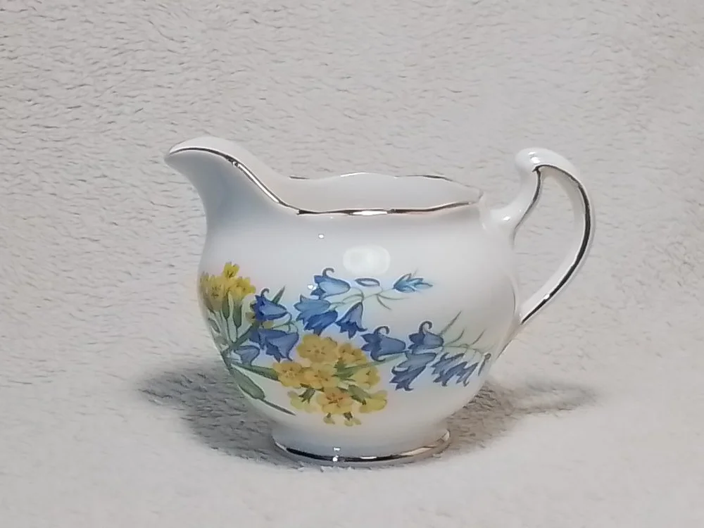 A white porcelain creamer with blue and yellow floral patterns and silver trim.
