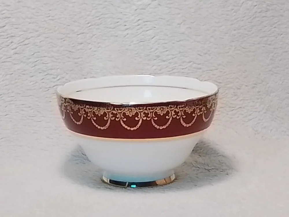 A decorative porcelain bowl with a gold and brown pattern around the top edge, resting on a fluffy white surface with a textured white background.