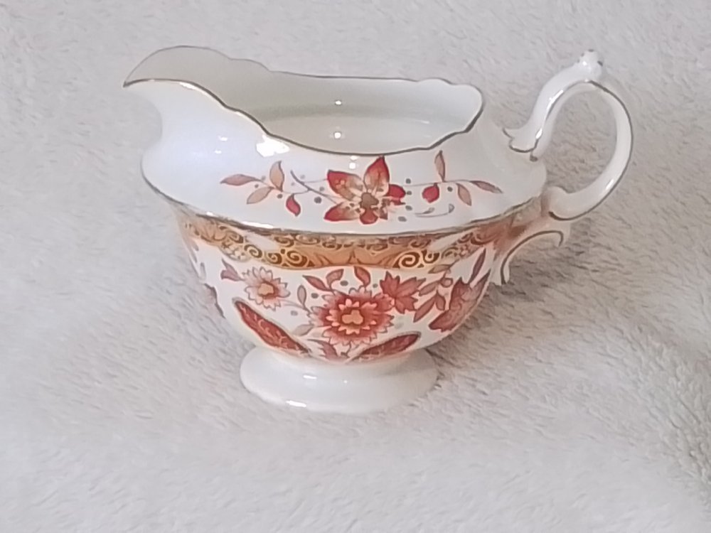 A decorative porcelain gravy boat with floral and gold accents, placed on a textured white surface.
