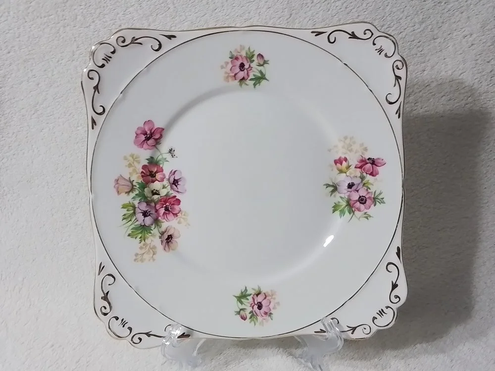 Decorative porcelain plate with a floral pattern and black scroll accents around the border, displayed on a clear stand.