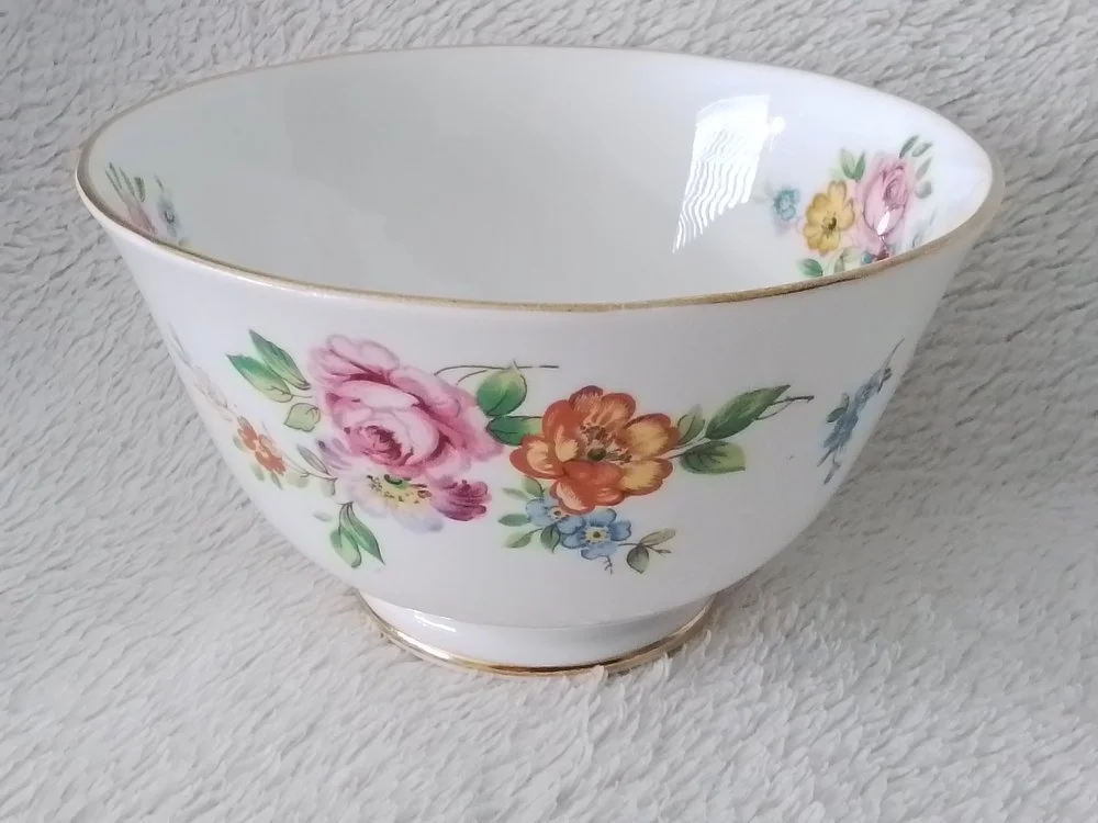 A white porcelain bowl with floral pattern and gold trim, featuring pink, orange, yellow, and blue flowers with green leaves.