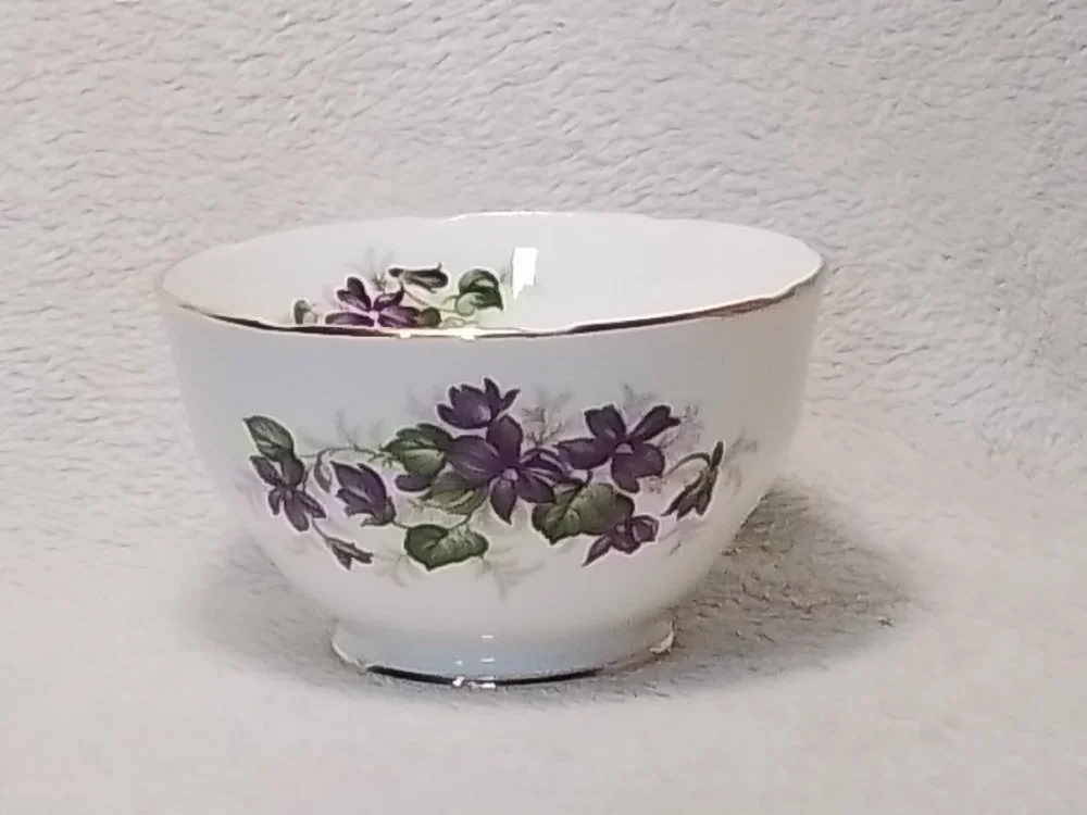A white porcelain bowl with purple and green floral pattern, placed on a white textured surface.