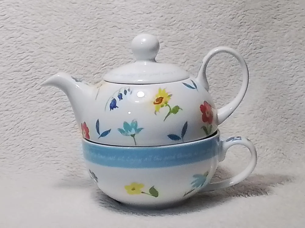 A floral teapot stacked on top of a floral teacup and saucer, all with matching colorful flower patterns.