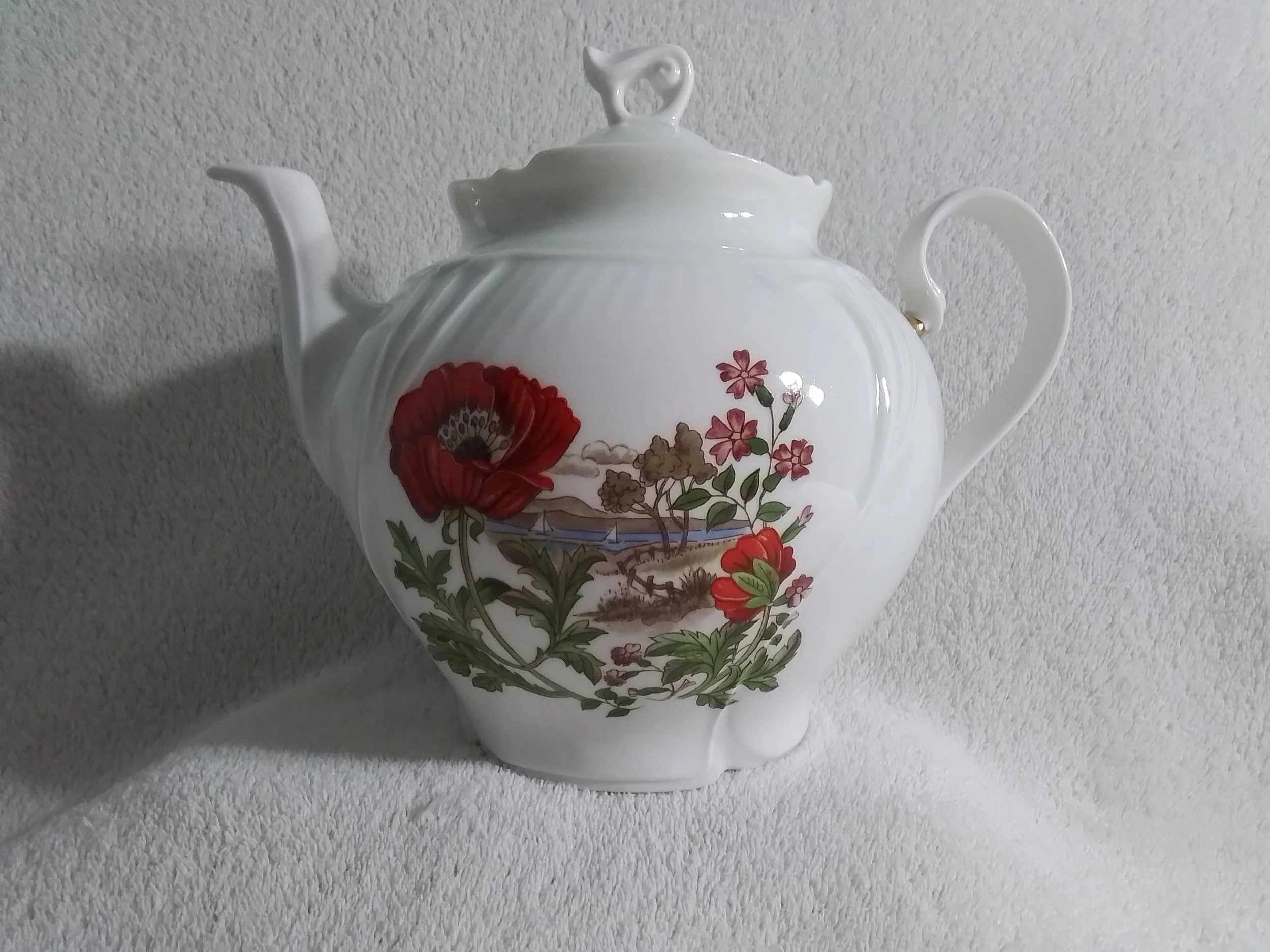 White porcelain teapot with painted red and pink flowers and a scenic landscape.