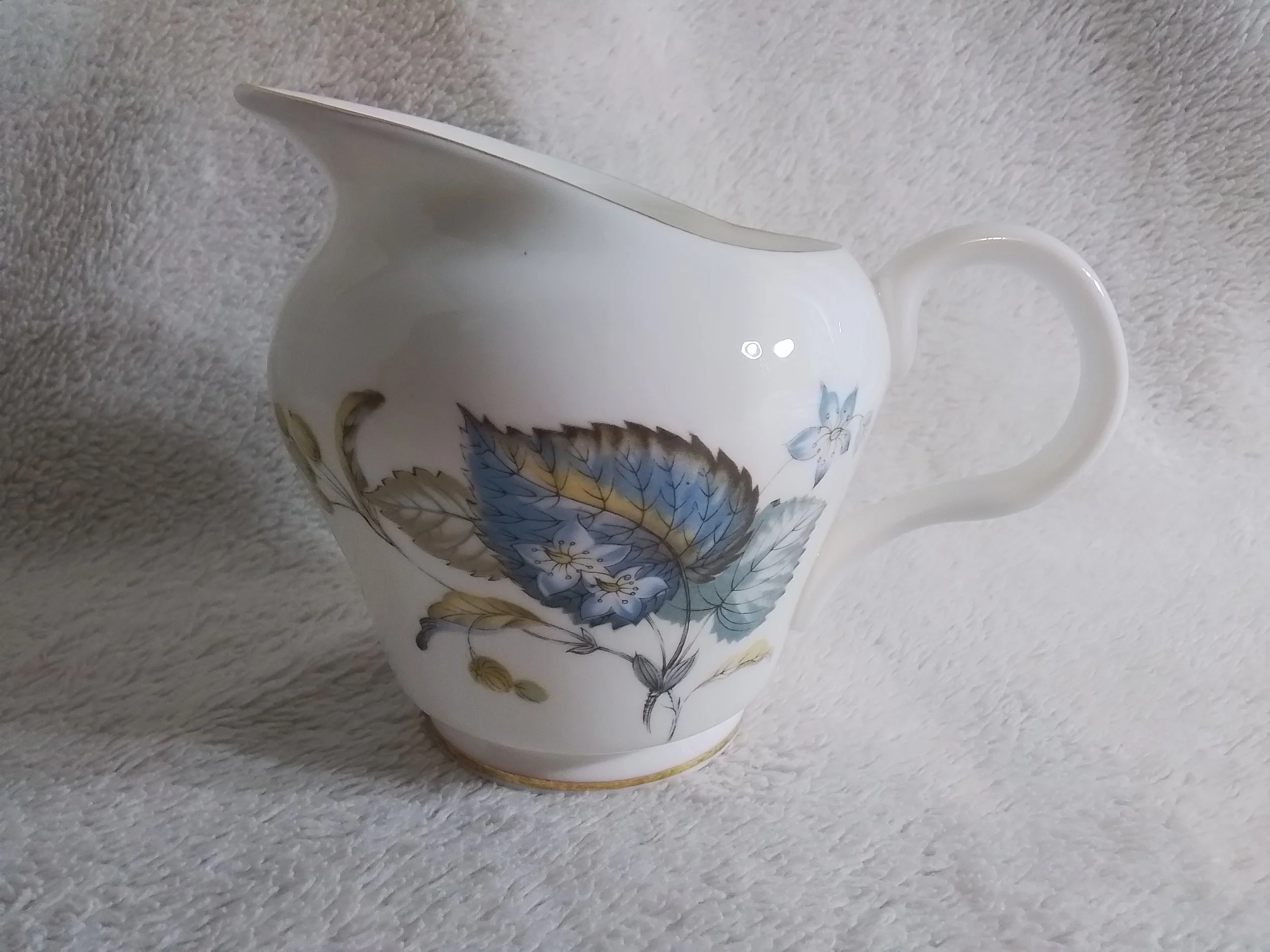White ceramic creamer with blue and yellow floral design, placed on a textured white surface.