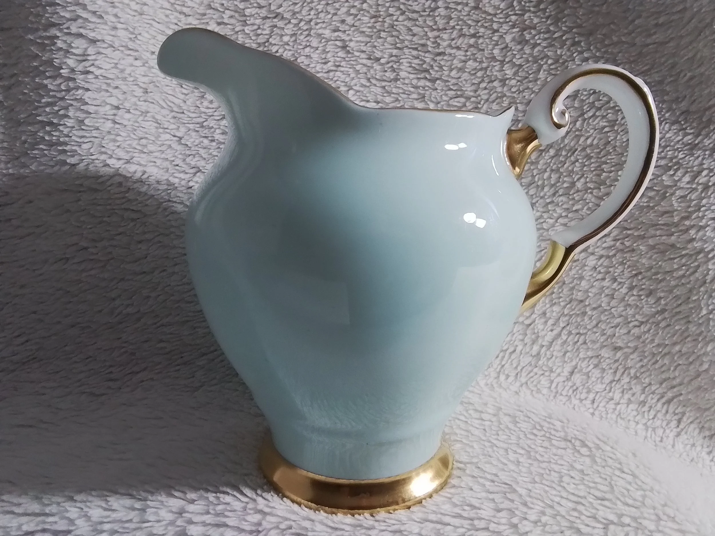 White ceramic pitcher with gold accents on the handle and base, placed on a textured gray surface.